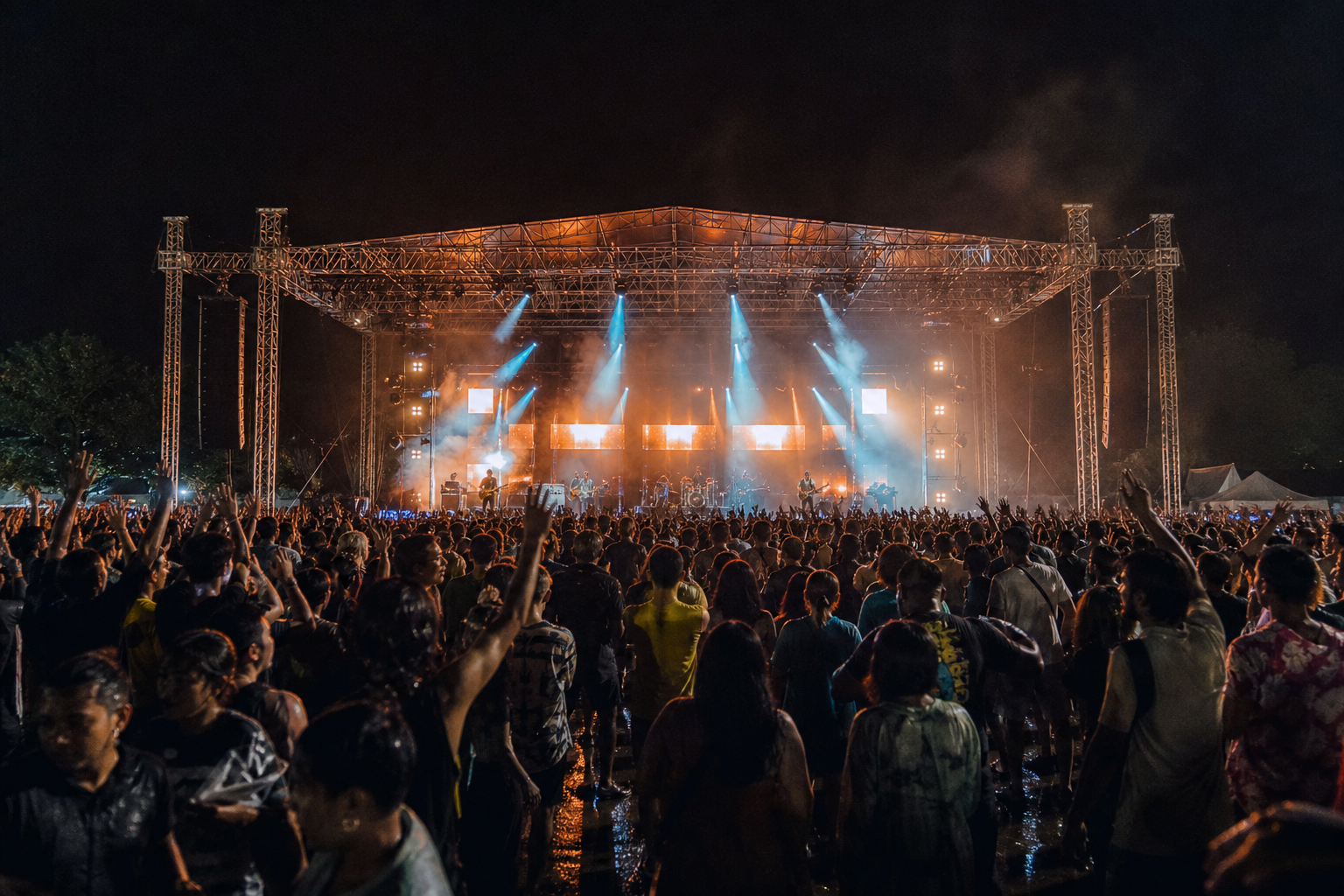 Crowd facing a large illuminated music festival stage at night